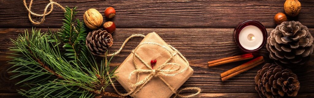 Photo illustrant un cadeau de Noël, accompagné d'une bougie, de pommes de pin et de bâton de cannelle